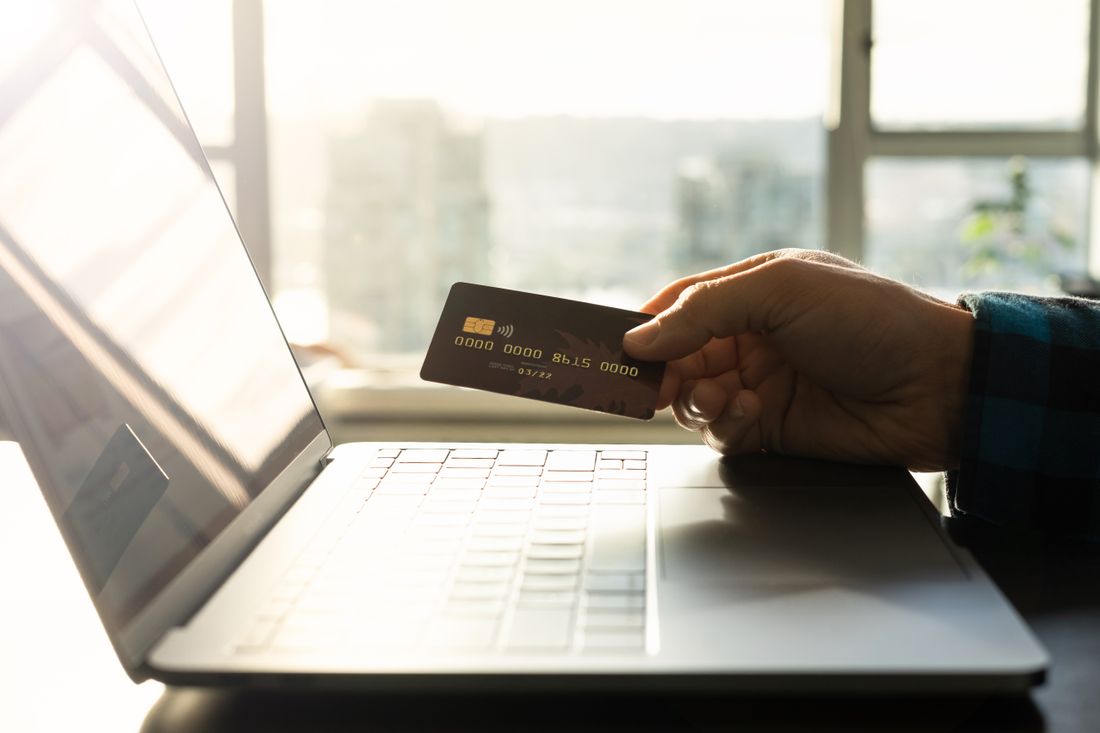 Una mano tiene una carta di pagamento davanti a un computer portatile